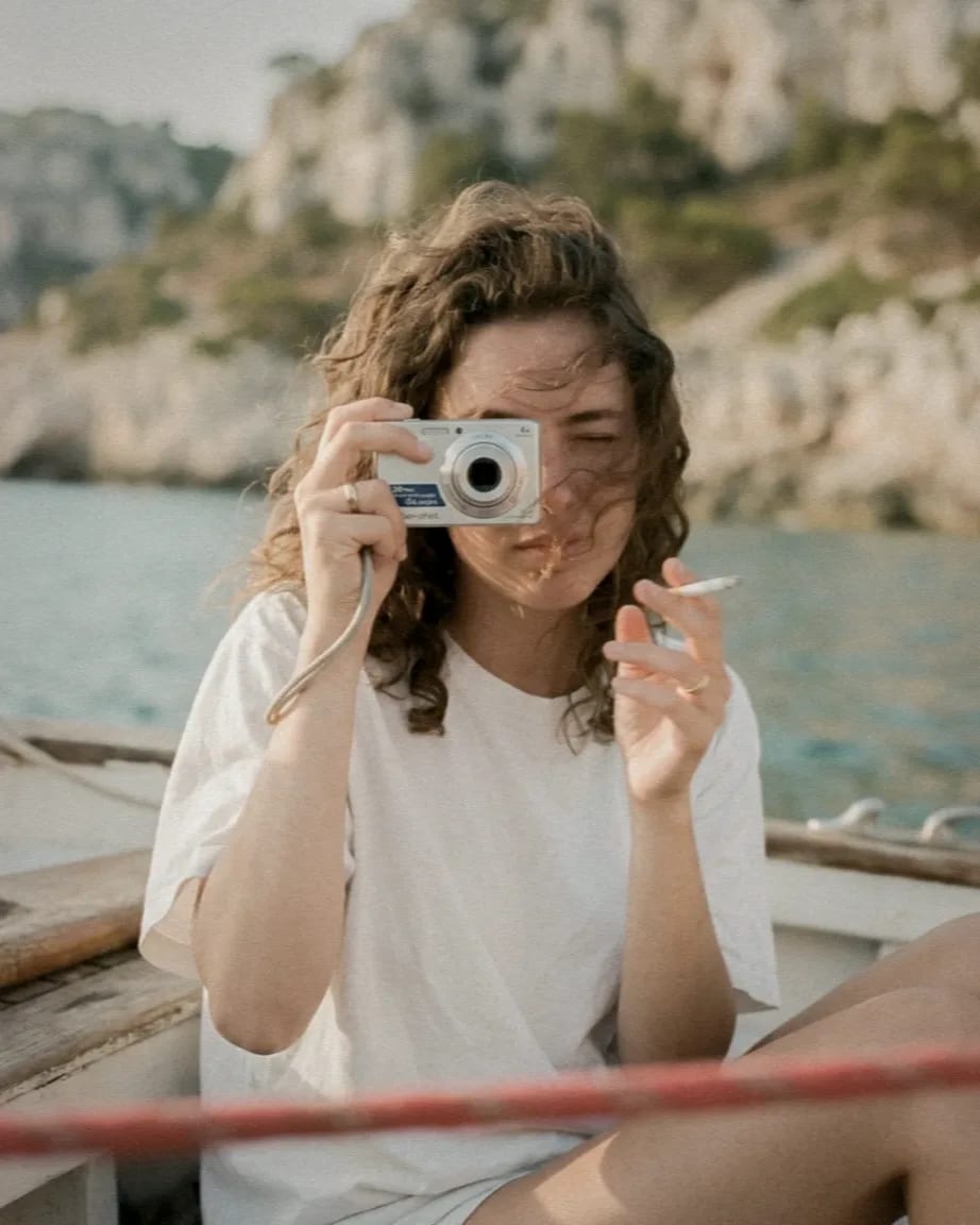 Una chica a bordo de un barco saca una foto con una cámara compacta, con acantilados detrás